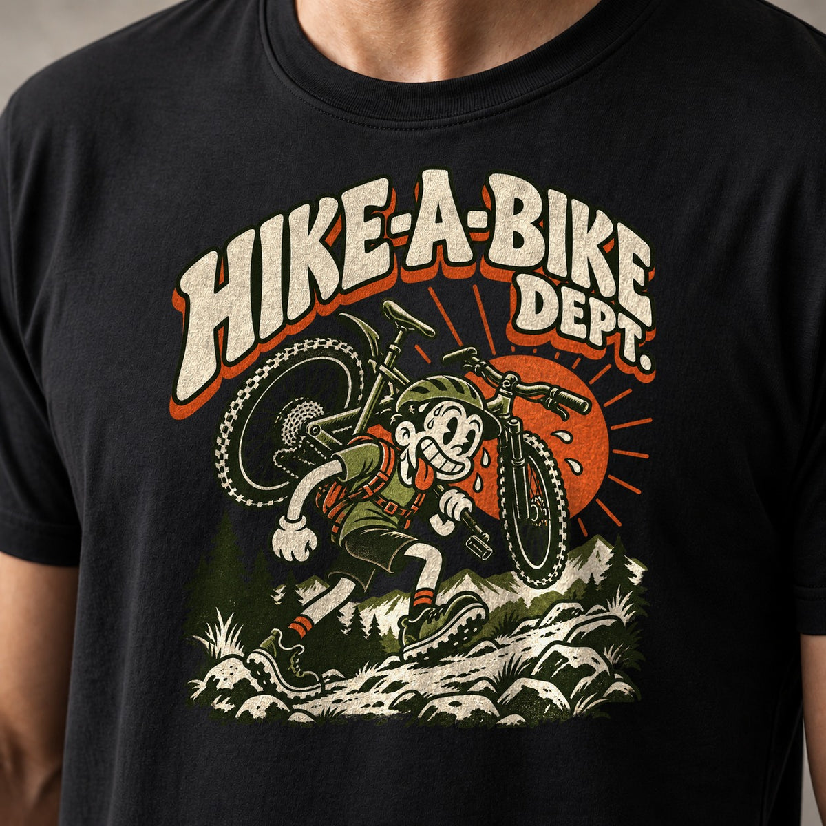 Hike-A-Bike Dept. retro cartoon mountain bike t-shirt in Black — rubber-hose rider carrying a bike on the shoulders up a rocky trail under an orange sun — close-up of the print