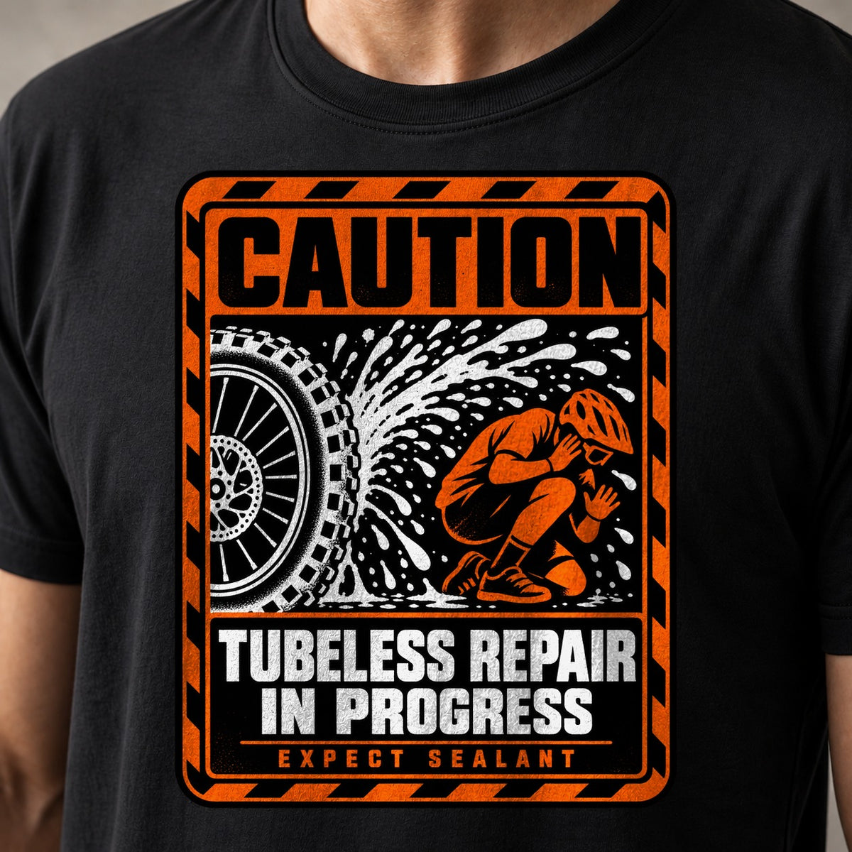 Caution Tubeless Repair In Progress funny mountain bike t-shirt in Black — orange hazard sign with a tire spraying sealant at a crouching rider — close-up of the print